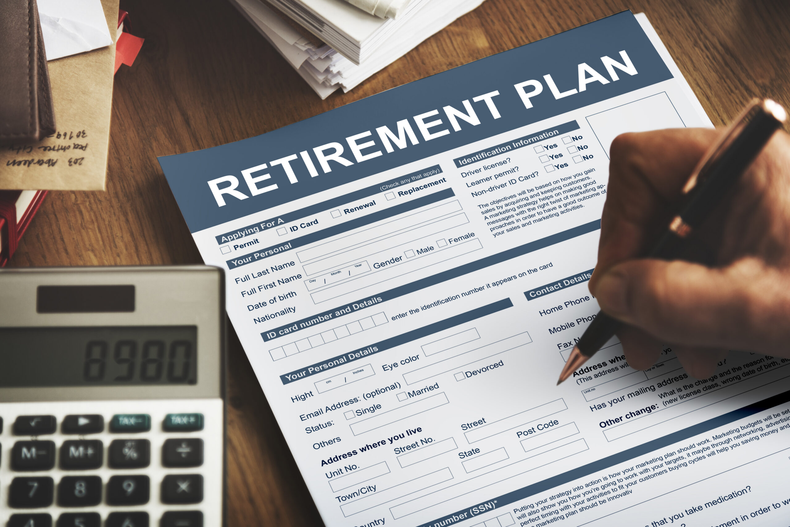 Person with pen writing on retirement plan forms that are on a desk.