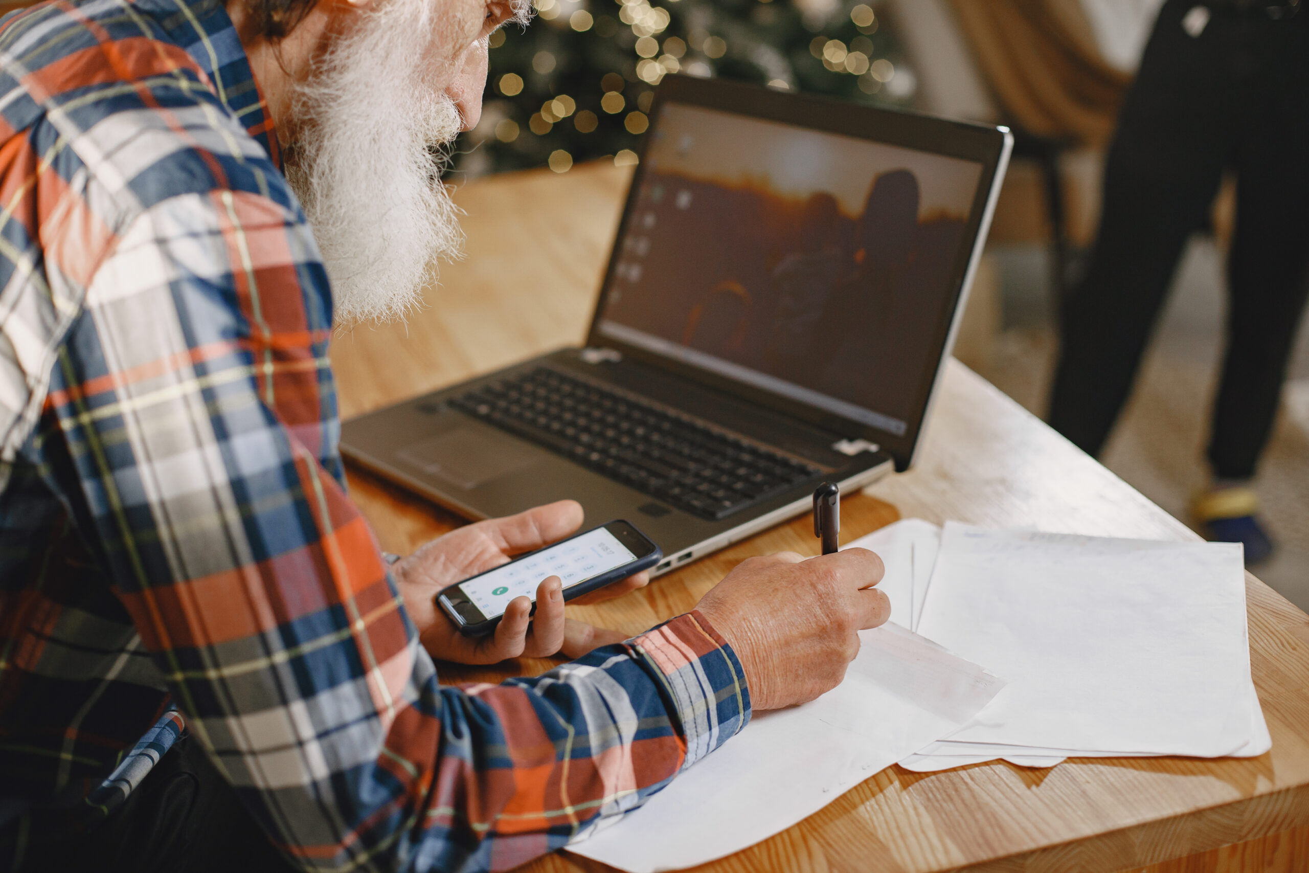 man reviewing document oh phone with laptop open.
