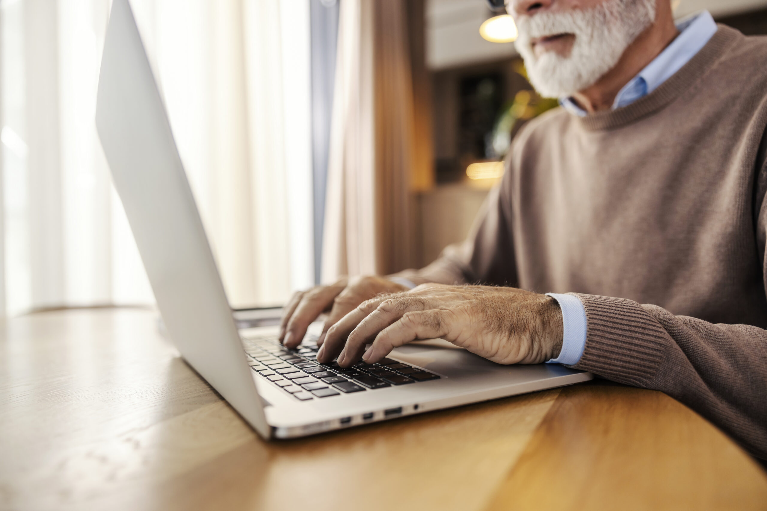 Close up of older trendy executive sitting at home and working remotely on a laptop.
