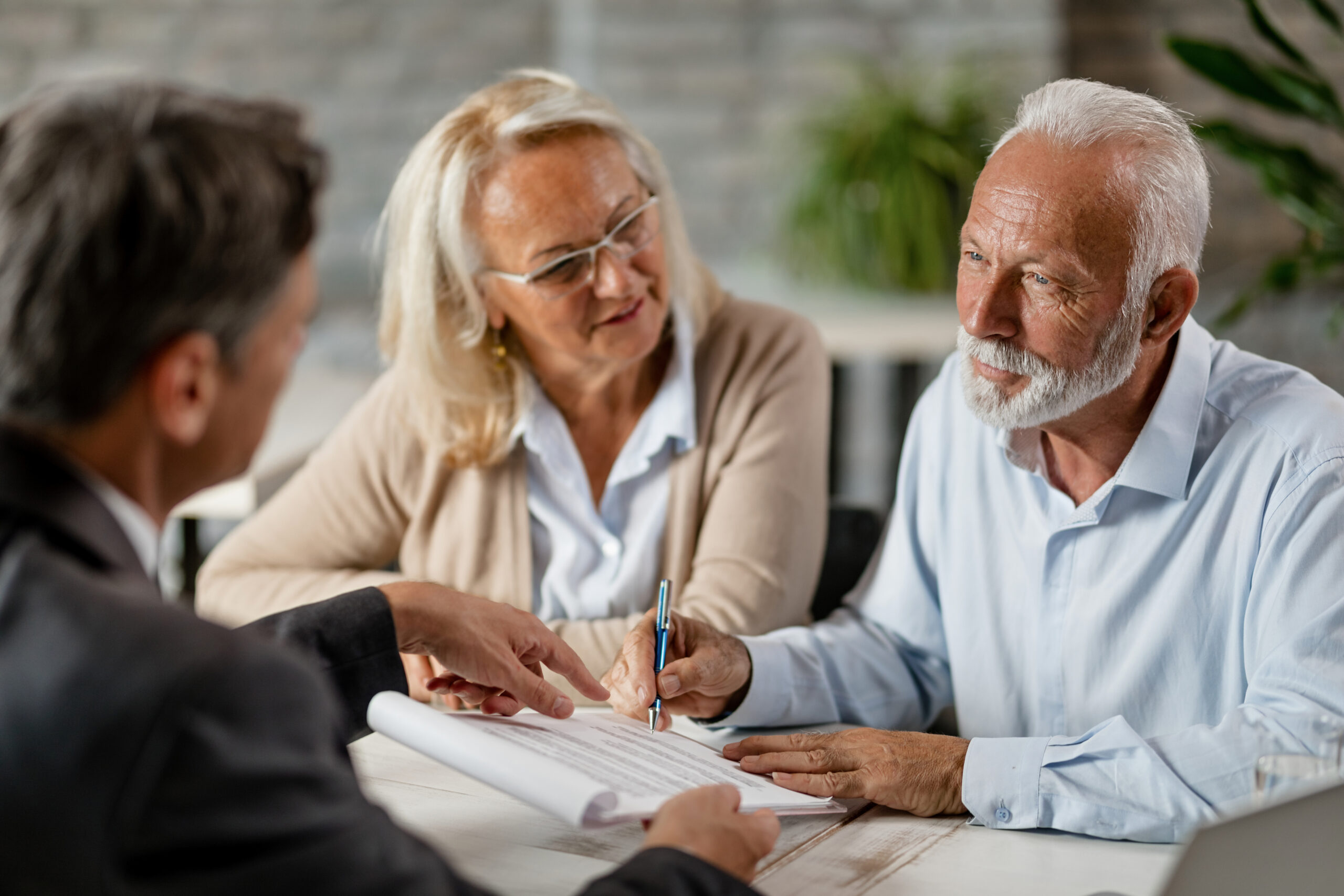 mature couple meeting with a man, signing papers.