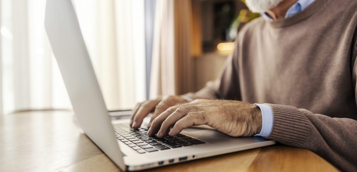 Close up of older trendy executive sitting at home and working remotely on a laptop.