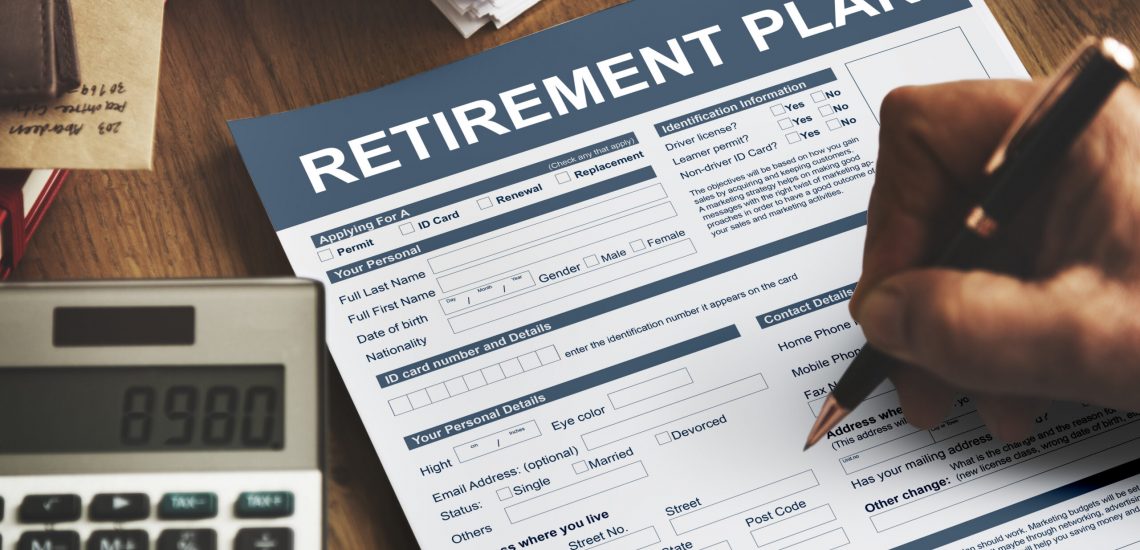 Person with pen writing on retirement plan forms that are on a desk.
